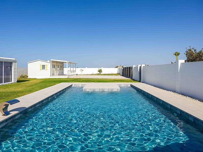 Piscinas con Ashen Zona de piscina azul en un paisaje moderno con césped y casas blancas al fondo.